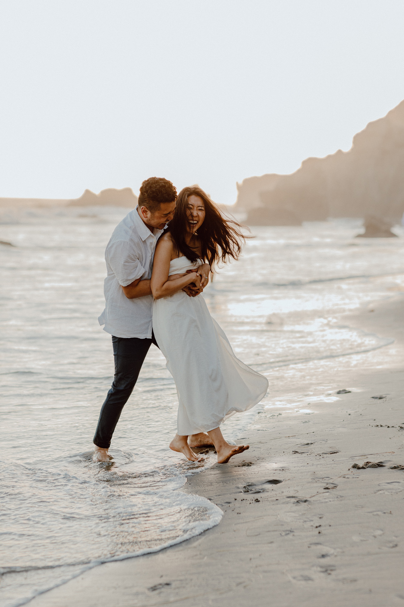 Couple playing and hugging on at the beach wearing white